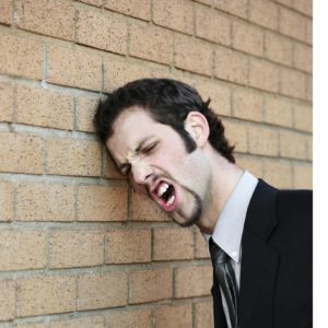 Young business man frustrated, hitting his head against the world passionately angry