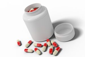 Red and white Capsules scattered around a white medicine container