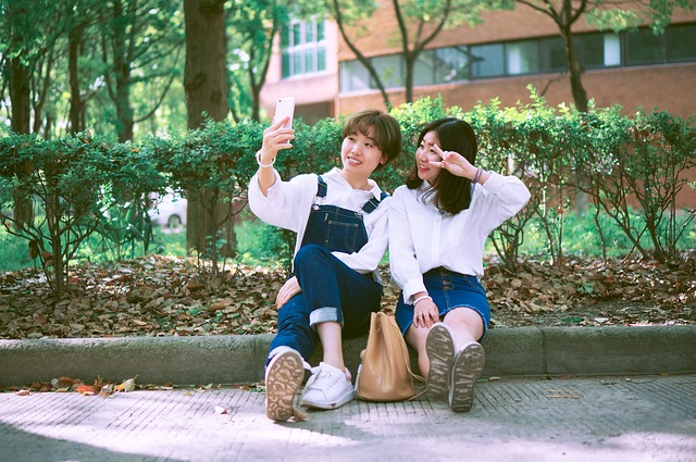 Two young Asian girl-students outside on college campus lawns taking a selfie.