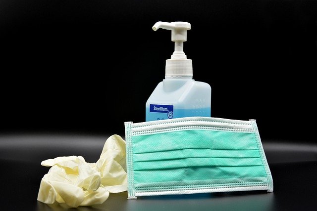 Hand disinfection soap, latex gloves and aquamarine surgical mask on black background