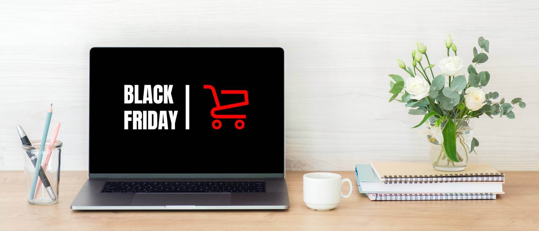 Laptop with “Black Friday” logo on wood desk with flowers, coffee cup and stationery.