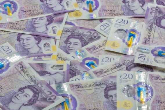 pile of british currency featuring the image of queen elizabeth II used to illustrate warning of scam
